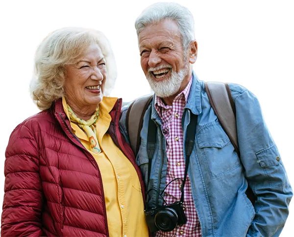 An elderly couple hiking in the woods with a camera.